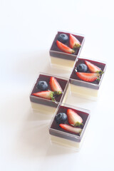 Vanilla Panna Cotta with Berry Compote, in square shot glasses, on a white background.