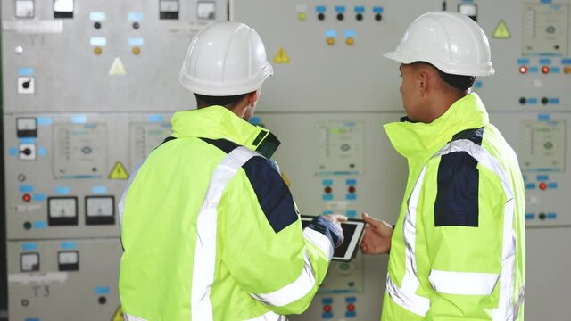 Electrical engineers checking control panel board with tablet. Electric industry, electrical energy production concept. High voltage power station