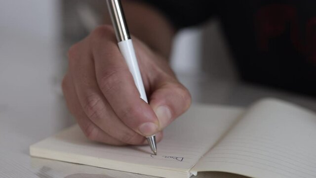 Male hand writing on a piece of paper. Writing essay or letters. Doing homework. Learning concept