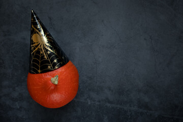 Close up of halloween pumpkin in a black paper cap with a spider on a dark background. Halloween, decoration and theme party concept.