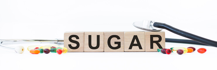 Sugar inscription on wooden cubes on a white background next to scattered tablets and stethoscope