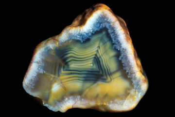 A sample of a concentrically layered blue-yellow-green agate stone on a black background.