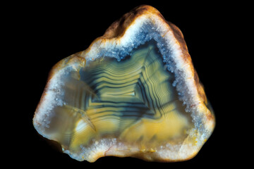 A sample of a concentrically layered blue-yellow-green agate stone on a black background.