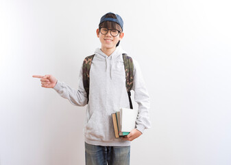 Asian teen boy students carrying a backpack and books pointing finger standing on white background.