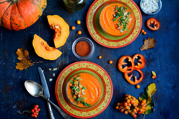 Top view of serving orange plates with bright pumpkin soup, spices, herbs, pumpkins on a dark blue background. Top view