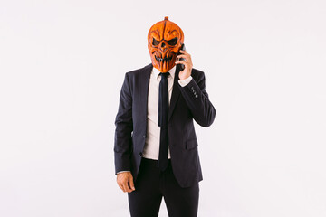 Man dressed in a suit jacket, blue tie and Jack-o-lantern pumpkin mask, talking on the mobile phone, like crazy. Halloween and carnival celebration concept.