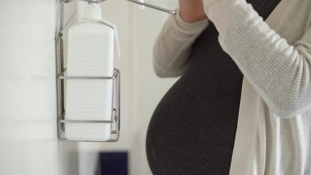 Close Up Young Pregnant Woman Treats Disinfects Hands With Antiseptic Before Medical Control On Hospital. Visit Gynecologist Doctor At Clinic. Examine Expectant Belly Baby Mother Healthcare Check Up