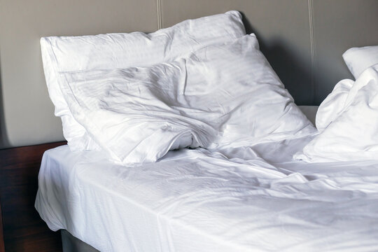 Closeup of unmade bed in the morning. White linen or bedclothes
