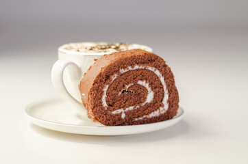 Chocolate sponge roll with a vanilla flavour filling and fresh coffee in the cup, chocolate swiss roll