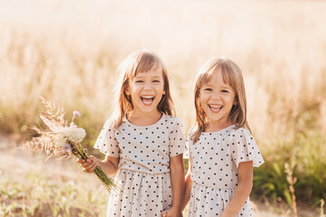 Two little happy identical twin girls playing together in nature in summer. Girls friendship and youth concept. Active children's lifestyle. - obrazy, fototapety, plakaty
