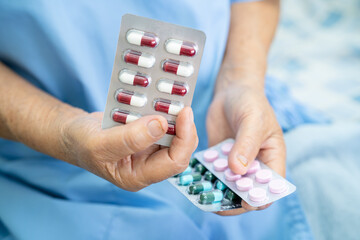 Asian senior woman patient holding antibiotics capsule pills in blister packaging for treatment infection patient in hospital, Pharmacy drugstore concept. Pharmacy drugstore concept.