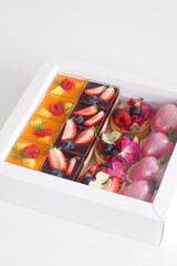 Sweet Gift Box with Berry Fruit and Tropical Fruit Panna Cotta, Fruit Tarts and Strawberries Glazed with Pink Chocolate, on a white background.