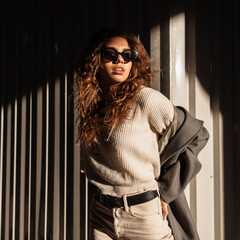 Fashion portrait of beautiful young stylish woman with curly hair and sunglasses in vintage sweater...