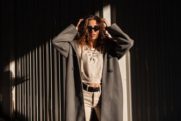 Stylish beautiful young curly-haired girl with fashion sunglasses in a fashionable long coat with a...