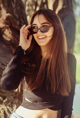 Beautiful toothy laughing woman looking happy in fashion sunglasses outdoors summer green trees background. Closeup portrait