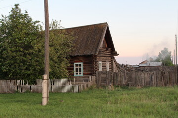 Fototapeta na wymiar Russian village, an old house on a green lawn at sunset. Summer in Siberia.