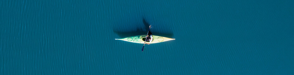 View from above, aerial view of a person paddling a canoe - kayak on the Cedrino Lake surrounded by the mountain range of Supramonte located northeast of the Gennargentu massif. Sardinia, Italy. - obrazy, fototapety, plakaty