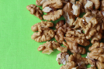 Top down view of shelled walnuts on a bright green table cloth. Nature food healthy snacks background, with copyspace to the left.