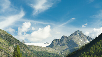 Blue sky with white clouds over italian alps and mountain peaks. On the left the glacier named 