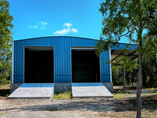 Large blue metal building on country side with open gates on blue  sky background. Steel construction.