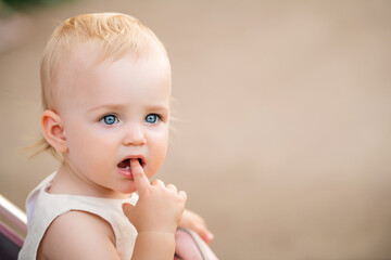 Portrait of blue-eyed baby sucking finger in her mouth, two first teeth are visible.