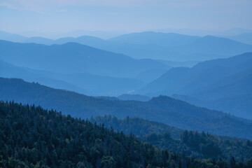 High peaks of beautiful dark blue mountain range landscape with fog and forest. Horizontal image.