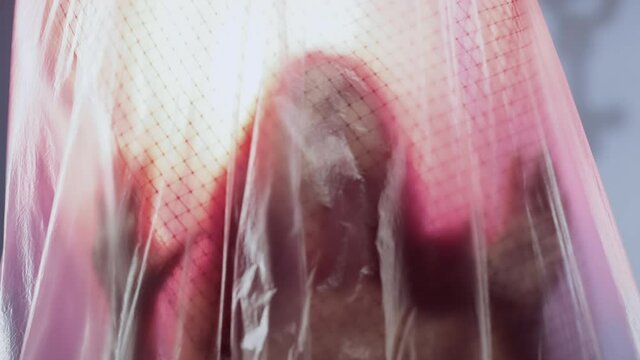 Human trafficking. Imprisonment problem. Isolation loneliness. Social issue. Defocused unhappy woman silhouette trapped behind cage plastic wrap on light out of focus background.