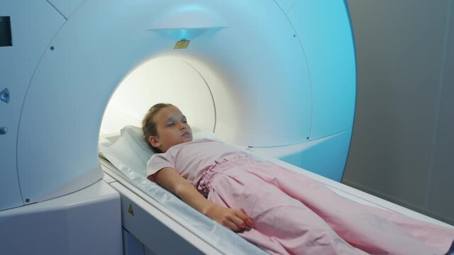 Slowmo shot of 9-year-old girl getting inside magnetic resonance imaging scanner for examination in modern high-tech clinic