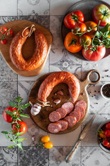 Smoked sausage on wooden boards with tomatoes, garlic and spices on a light tiled background