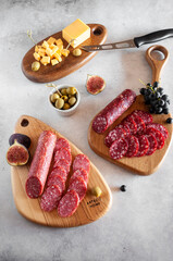 Salami with figs, cheese, olives and grapes on wooden boards on a light gray background