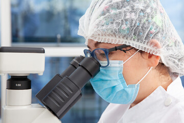 Young female scientist looking at samples under the microscope