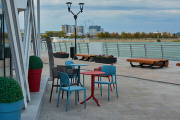 Small street cafe on the promenade. Table and chairs. Red and blue. Cityscape. Leisure.