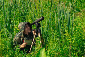 man wildlife researcher makes field observation with a spotting scope
