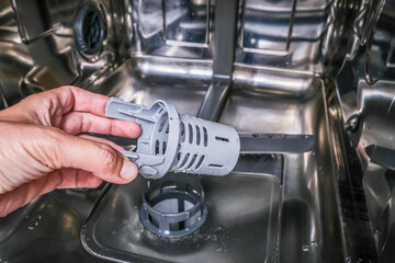 A hand taking out dishwasher filter to clean it, dis washer cleaning concept, kitchen home appliances care and maintenance
