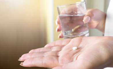 close up hand woman taking pill take a medicine in hand holding a cup glass of drinking water.