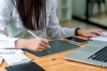 Close-up of a businesswoman hand holding a pen with a laptop document tablet placed at the office.