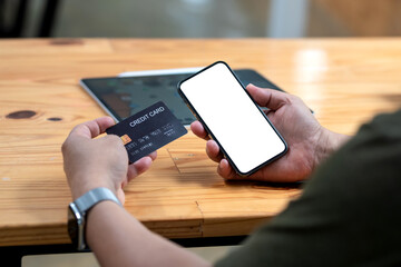 Close-up of man holding smartphone blank white screen with credit card online shopping. Mock up.