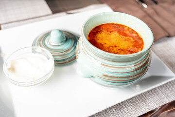 soup borscht in a pot with sour cream on a wooden table in a restaurant, traditional Ukrainian borscht, selective focusing