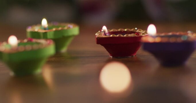 Four lit candles in decorative clay pots on wooden table top, bokeh flame in foreground