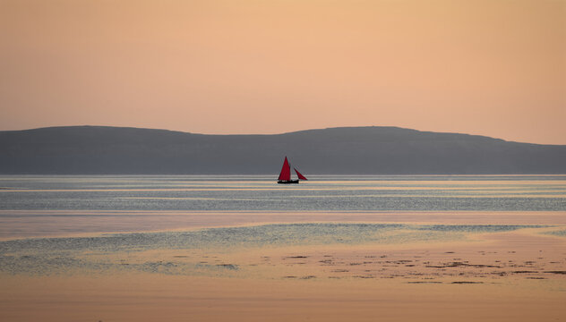 Beautiful orange sunset scenery with fishing boats named Galway hooker at Ballyloughane beach in Galway, Ireland 