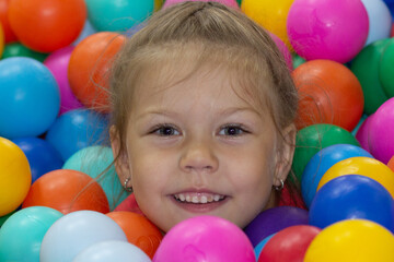Fototapeta na wymiar Head of happy caucasian little girl of five years old among multicolor balls in play center