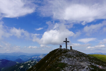 cross on the summit from a mountain with hikers and wide view