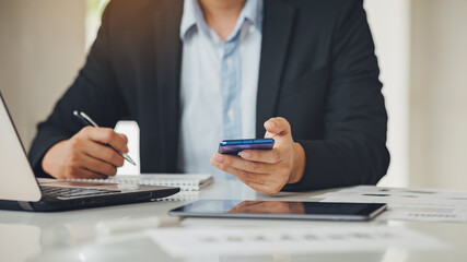 Fototapeta premium Young businessman working at the office for investment analyzing company financial report balance with smart phone. Concept for young entrepreneur and start up business.