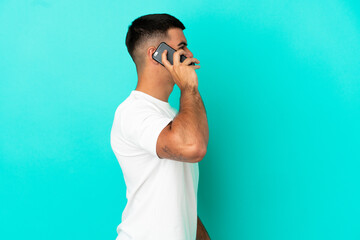 Young handsome man over isolated blue background keeping a conversation with the mobile phone with someone
