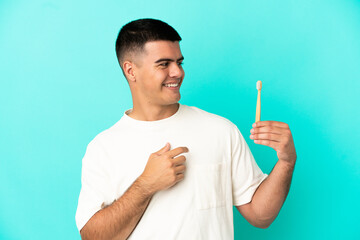Fototapeta premium Young handsome man brushing teeth over isolated blue background looking to the side and smiling