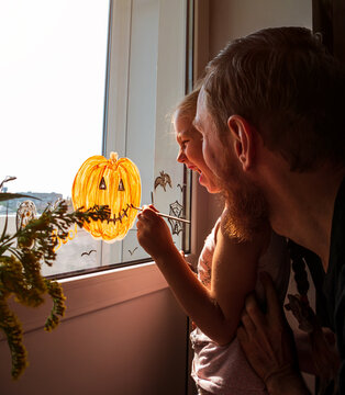 Child With Father Painting Pumpkin On Window Preparing To Halloween Little Girl With Dad Drawing Decorating Room