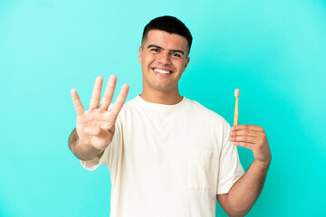 Fototapeta premium Young handsome man brushing teeth over isolated blue background happy and counting four with fingers