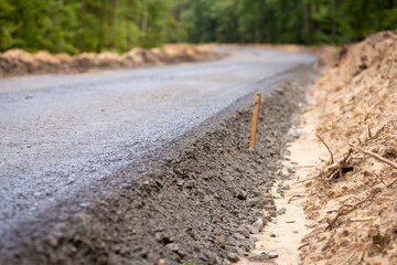 Close-up photo of new asphalt road pavement in the countryside. Constructing new high-quality road in the woods
