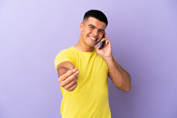 Fototapeta premium Young handsome man using mobile phone over isolated purple background making money gesture