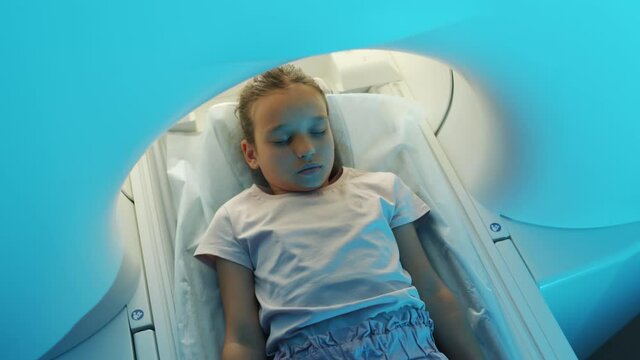 Slowmo top-view shot of 9-year-old girl lying with eyes closed on scanner table while having mri scanning procedure on high-tech medical equipment
